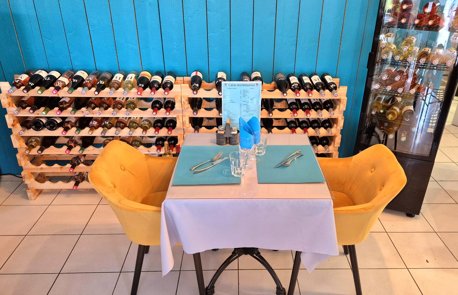 La salle : table dressée avec un sous-main orange, devant le mur de bouteilles de la cave à vins