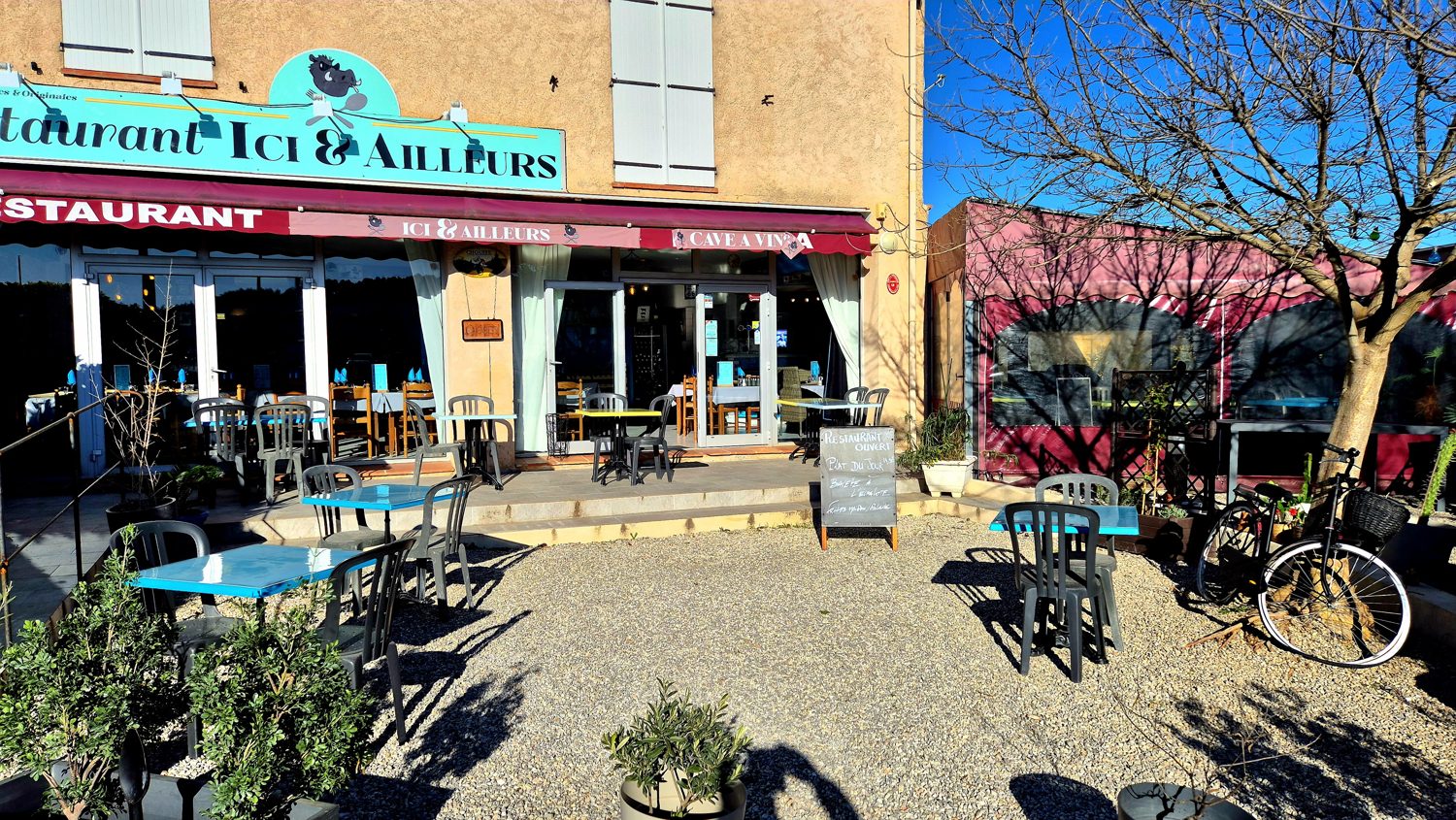 La terrasse du restaurant Ici & Ailleurs au soleil, façade jaune, vélos et tables dehors